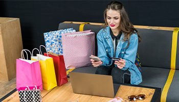 SEO 7 Young woman shopping online with laptop and credit card, surrounded by colorful shopping bags